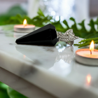 Glossy black obsidian pendulum on white marble beside candles