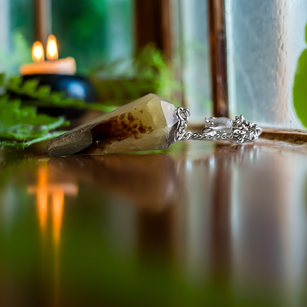 Mookaite jasper pendulum on a glossy table with plants and candlelight