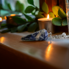 Blue sodalite pendulum on a wooden surface with plants and candlelight