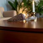 Rhodochrosite pendulum on a polished wooden table beside a candle